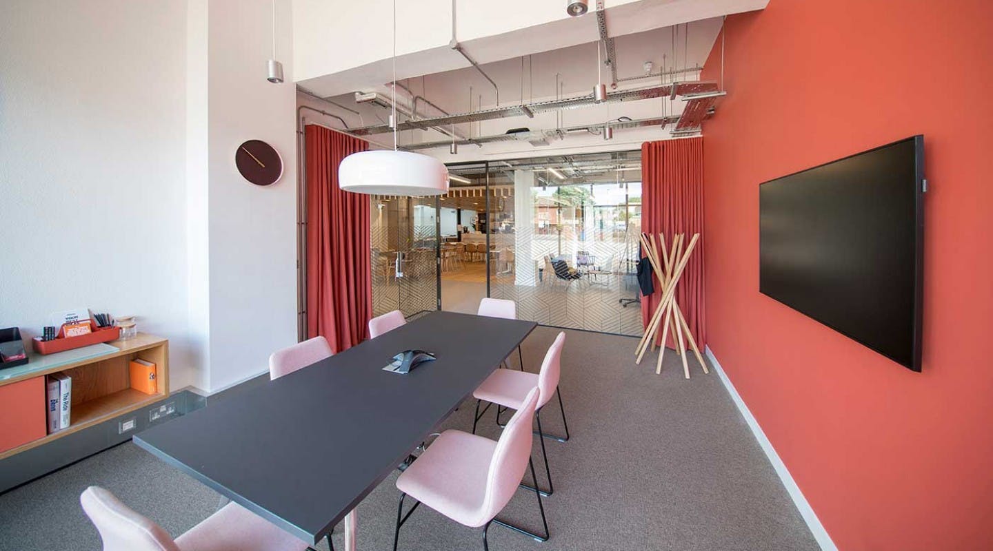 Modern meeting room with black table, pink chairs for collaborative events.