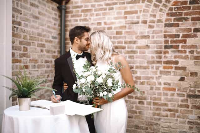 Couple celebrating wedding in The Colonnade, Pitzhanger Manor, with rustic brick backdrop.