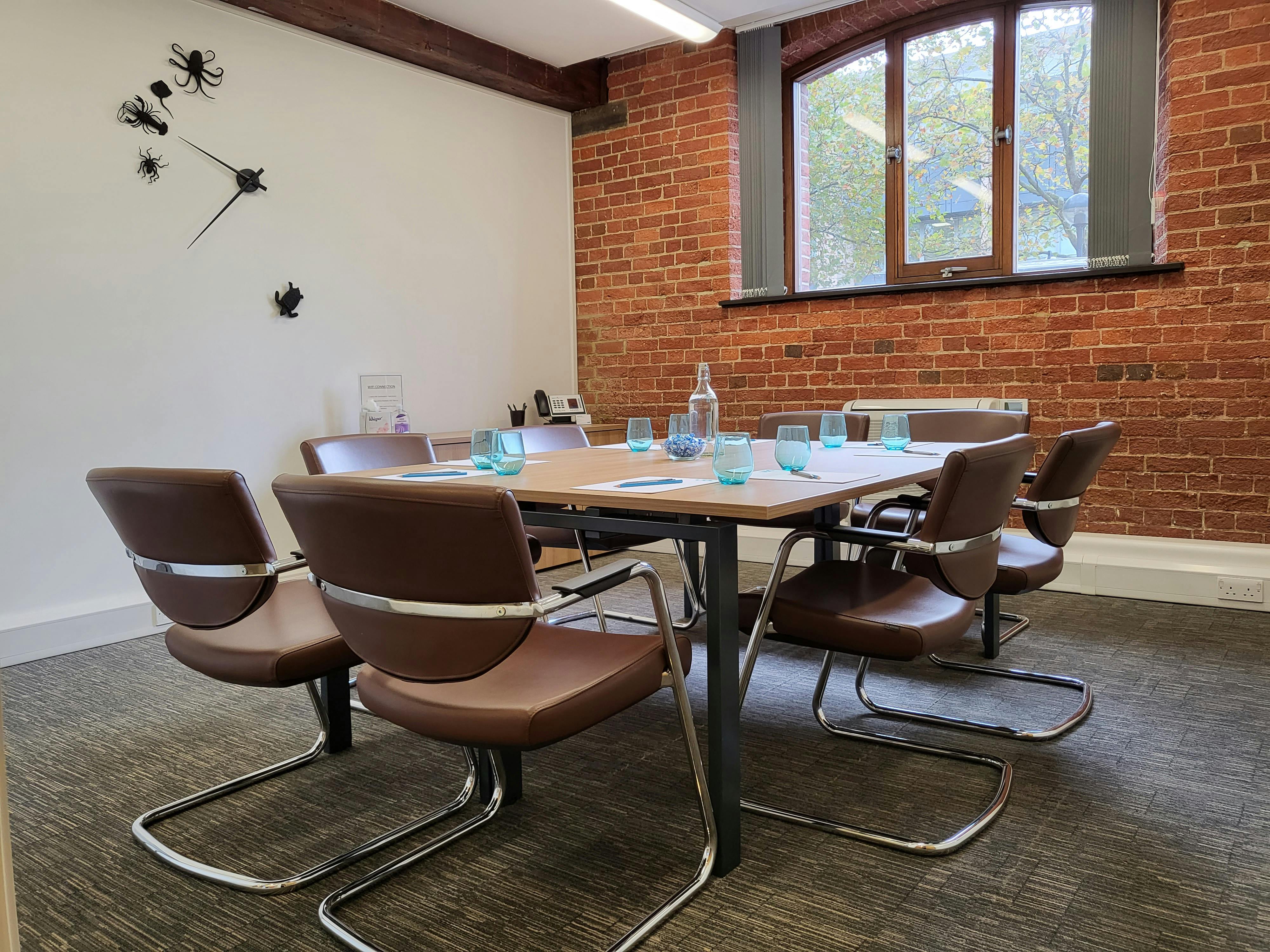 Modern meeting room in UBC Southampton with wooden table and exposed brick wall.