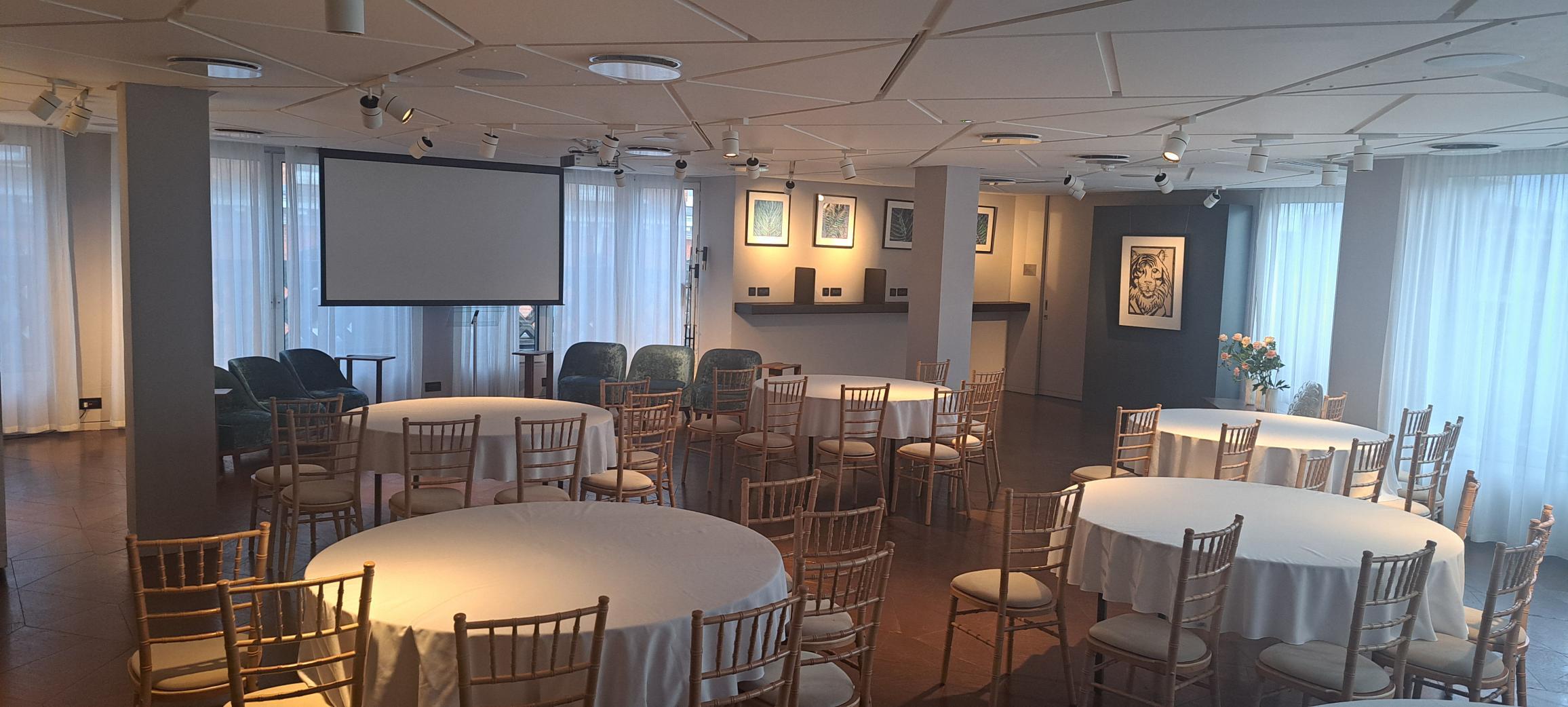 The Lounge at 12 Hay Hill: elegant meeting space with circular tables and projector screen. - Banner