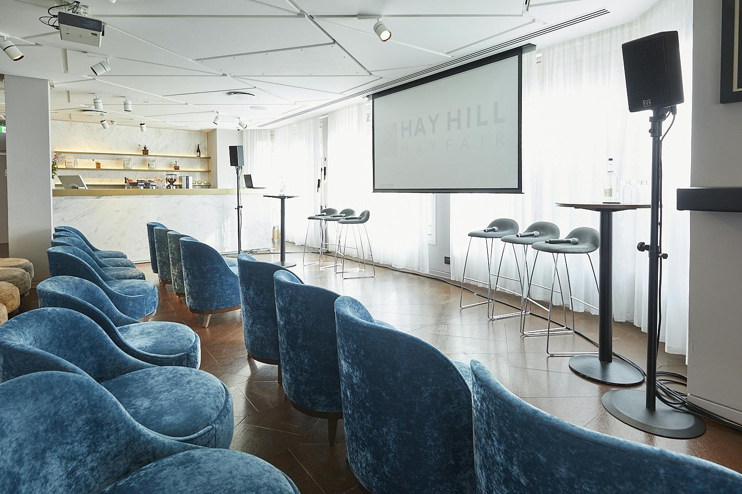 Modern event space with blue seating and large screen for presentations at 12 Hay Hill.