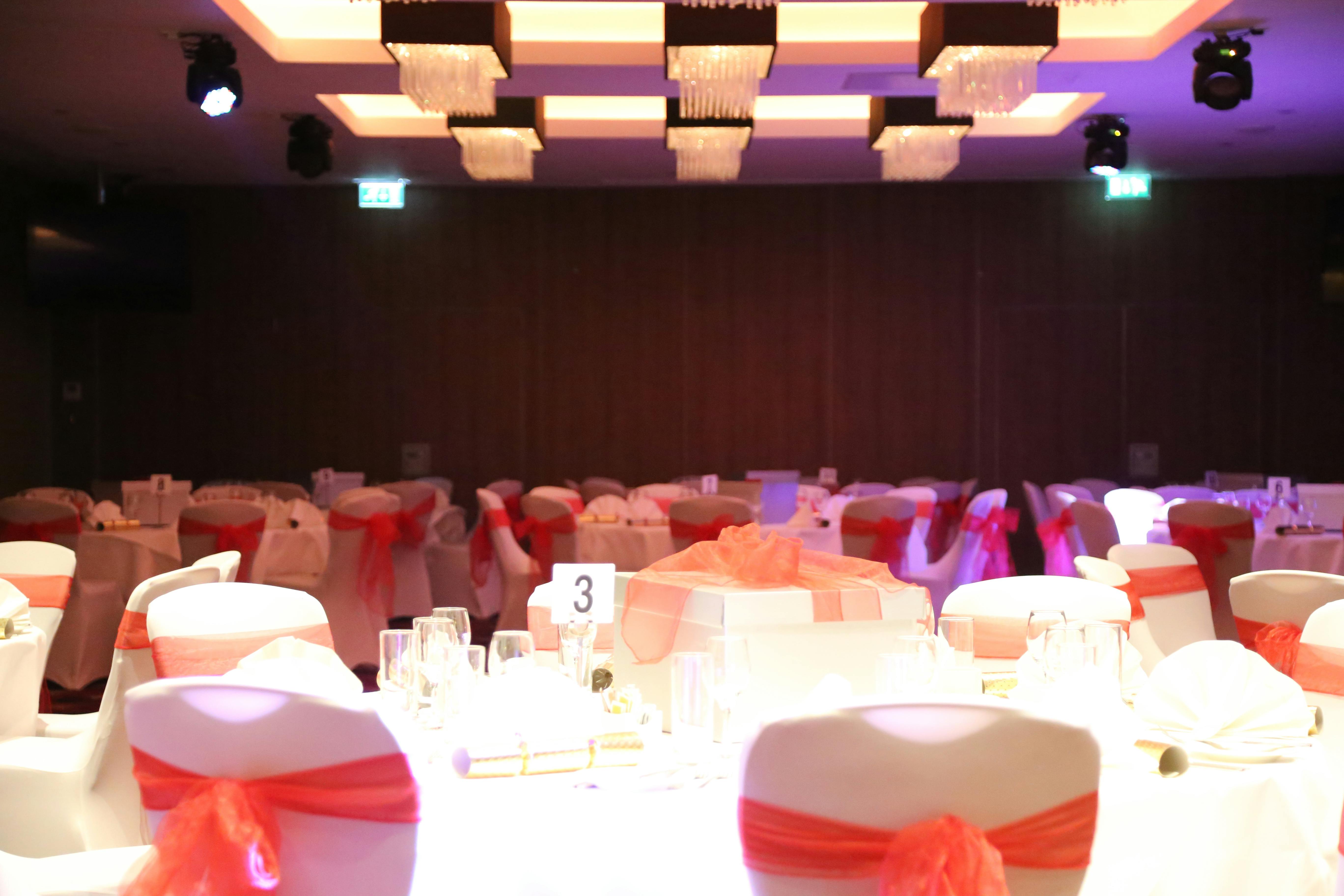 Elegant wedding banquet hall at Holiday Inn Kensington with red-sashed chairs.