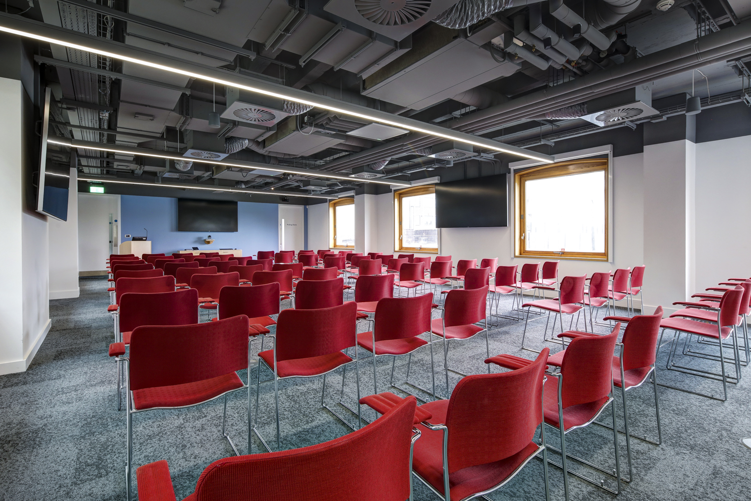 Modern meeting room with red chairs and dual screens for presentations and workshops. - Banner