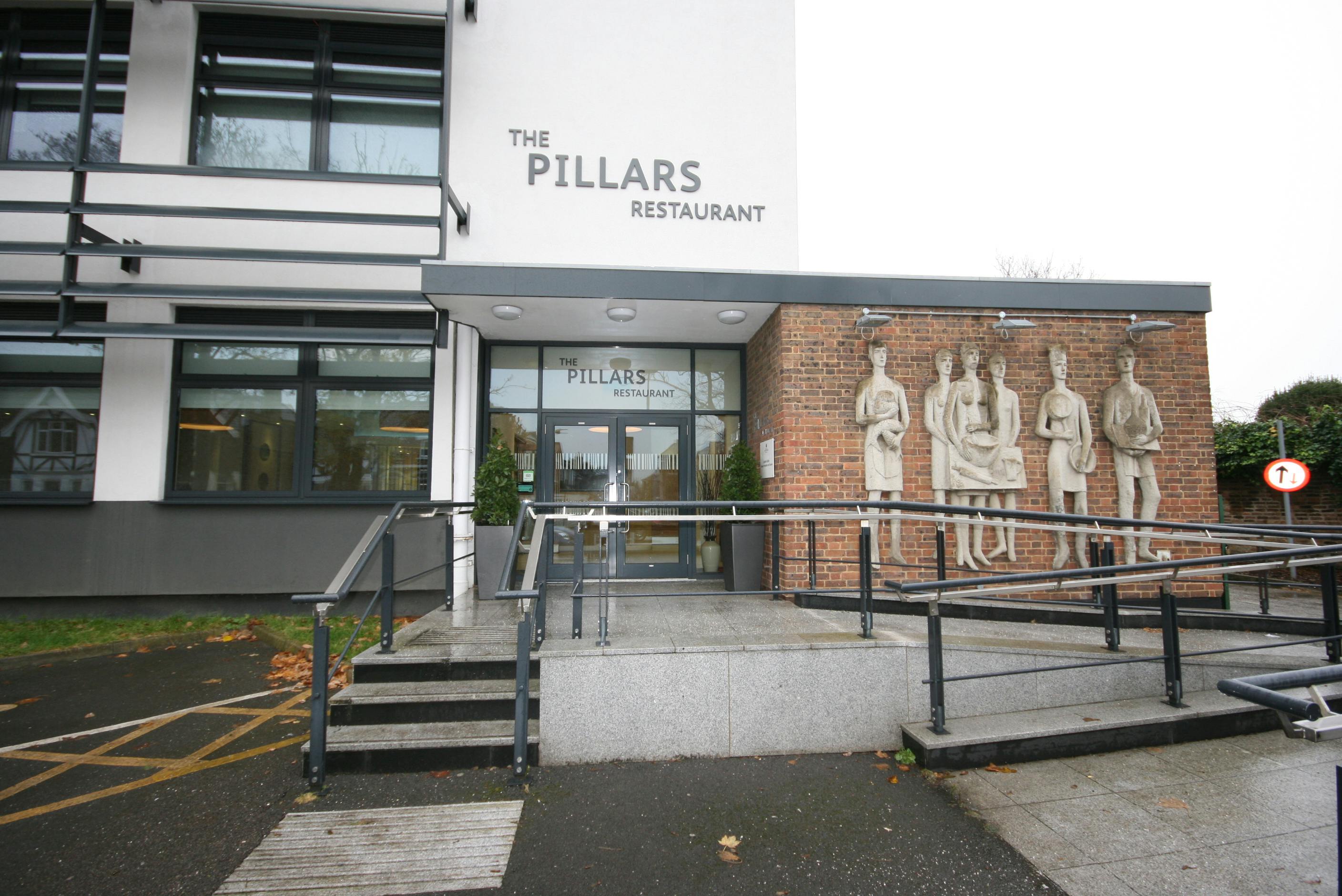 Pillars Kitchen entrance with modern facade and stone sculptures, ideal for events.