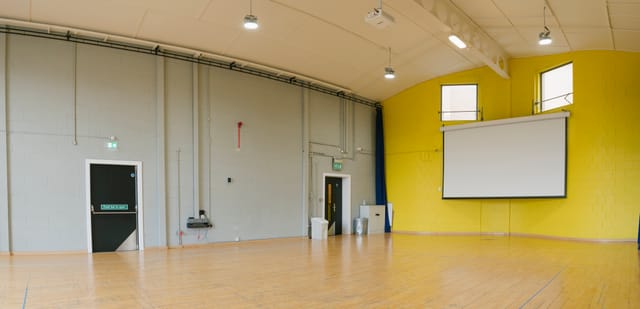 Versatile event space with wooden floor and yellow wall for workshops and presentations.