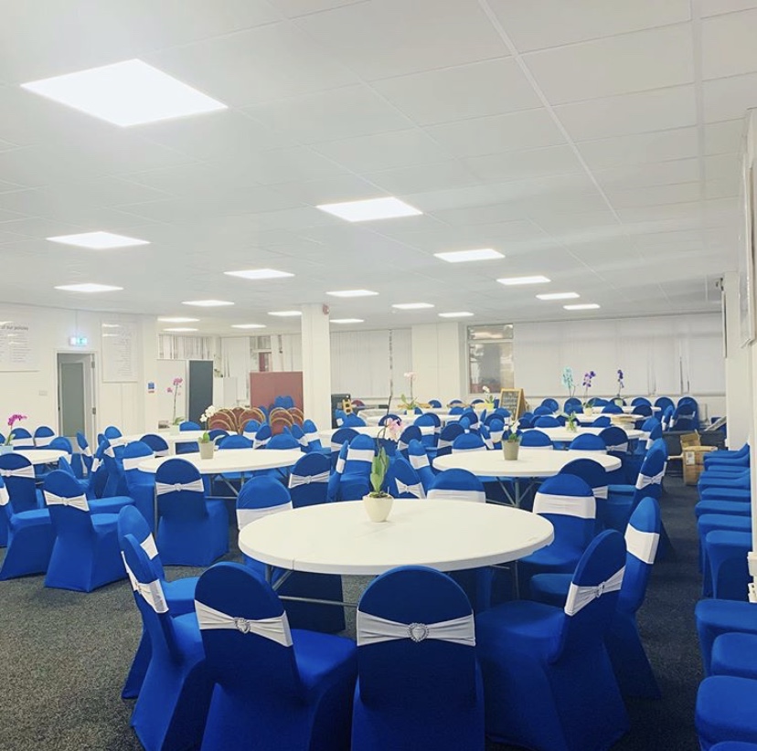 ACAA Hall setup for a meeting with round tables, blue chair covers, and white sashes. - Banner