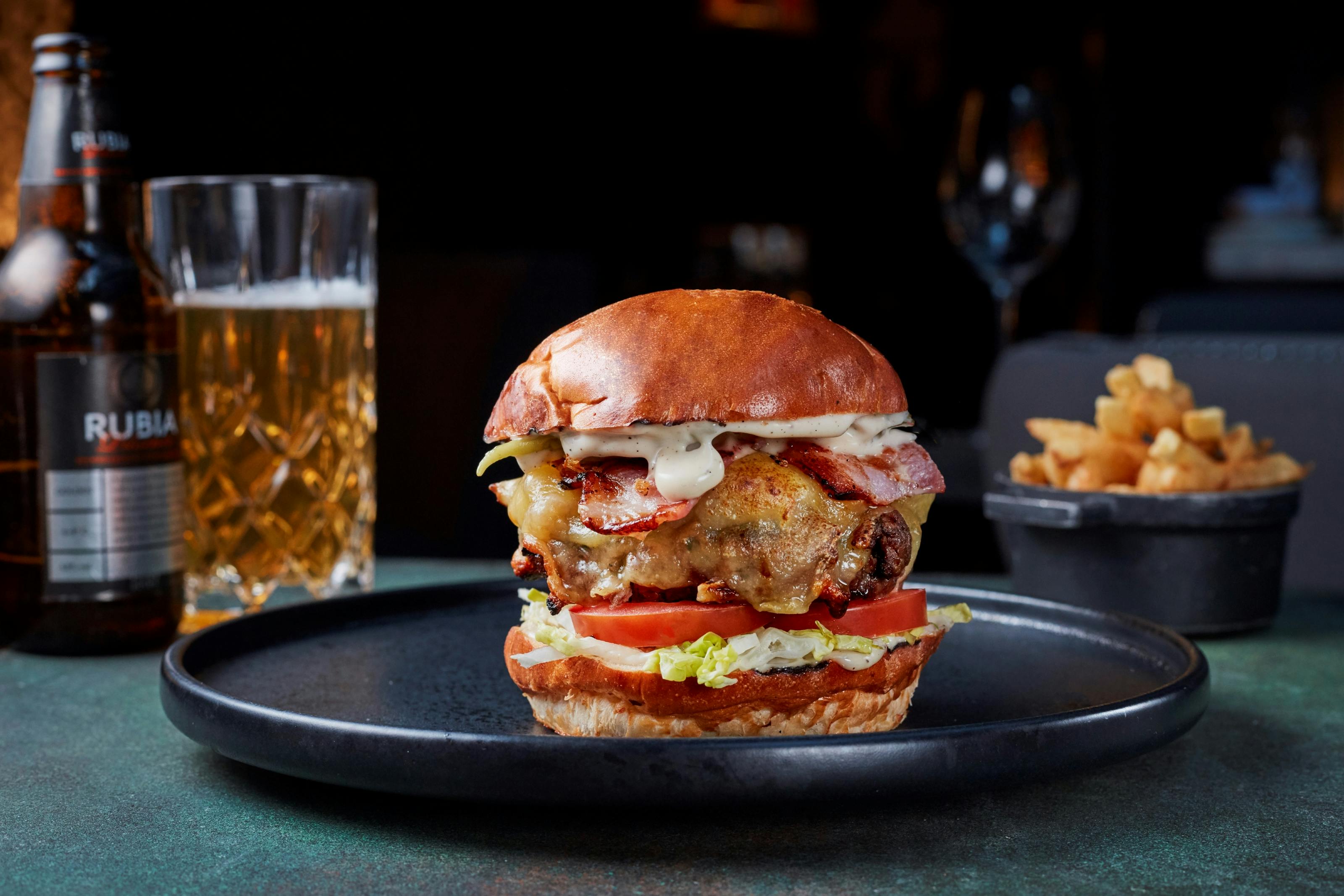 Gourmet burger with fries and beer in Spanish Room, perfect for events and catering.