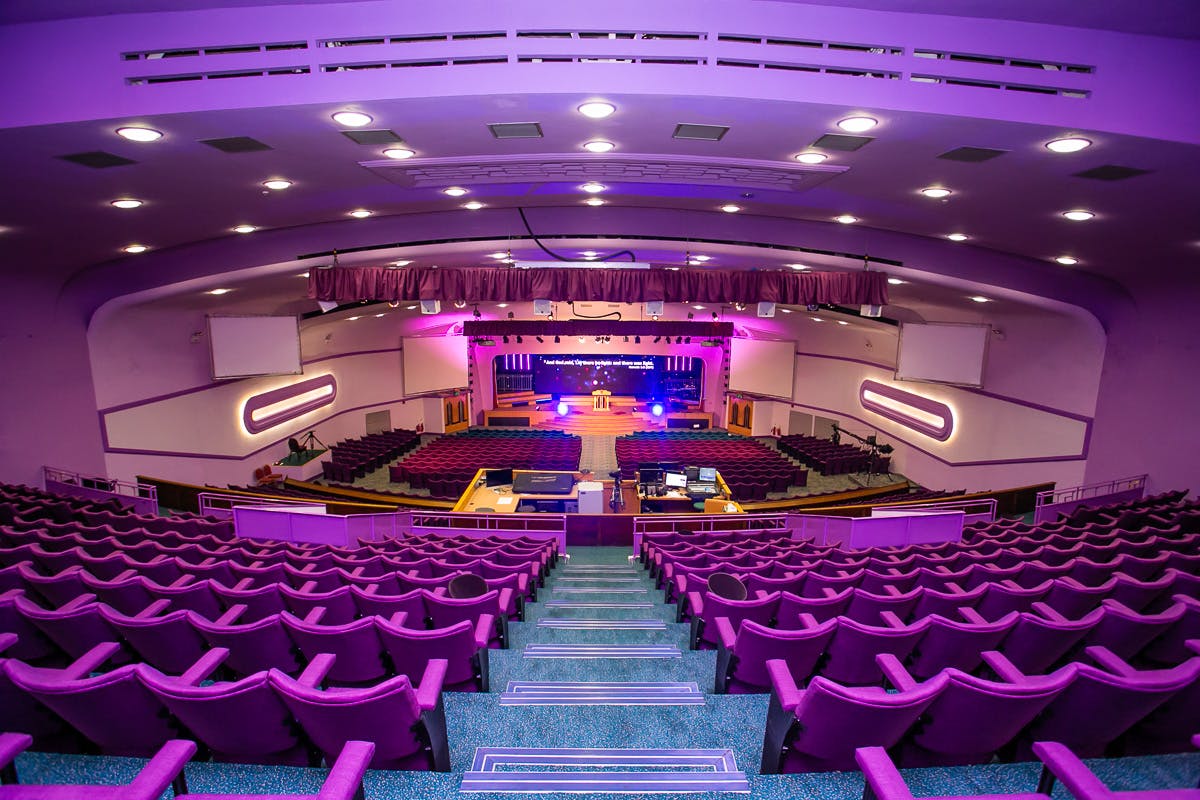 Spacious auditorium with tiered seating and purple lighting for conferences and events.