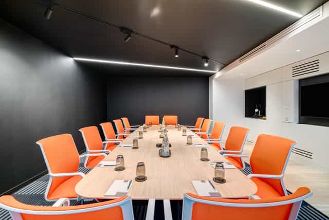Modern meeting room in Apex City of Bath Hotel with oval table and orange chairs.