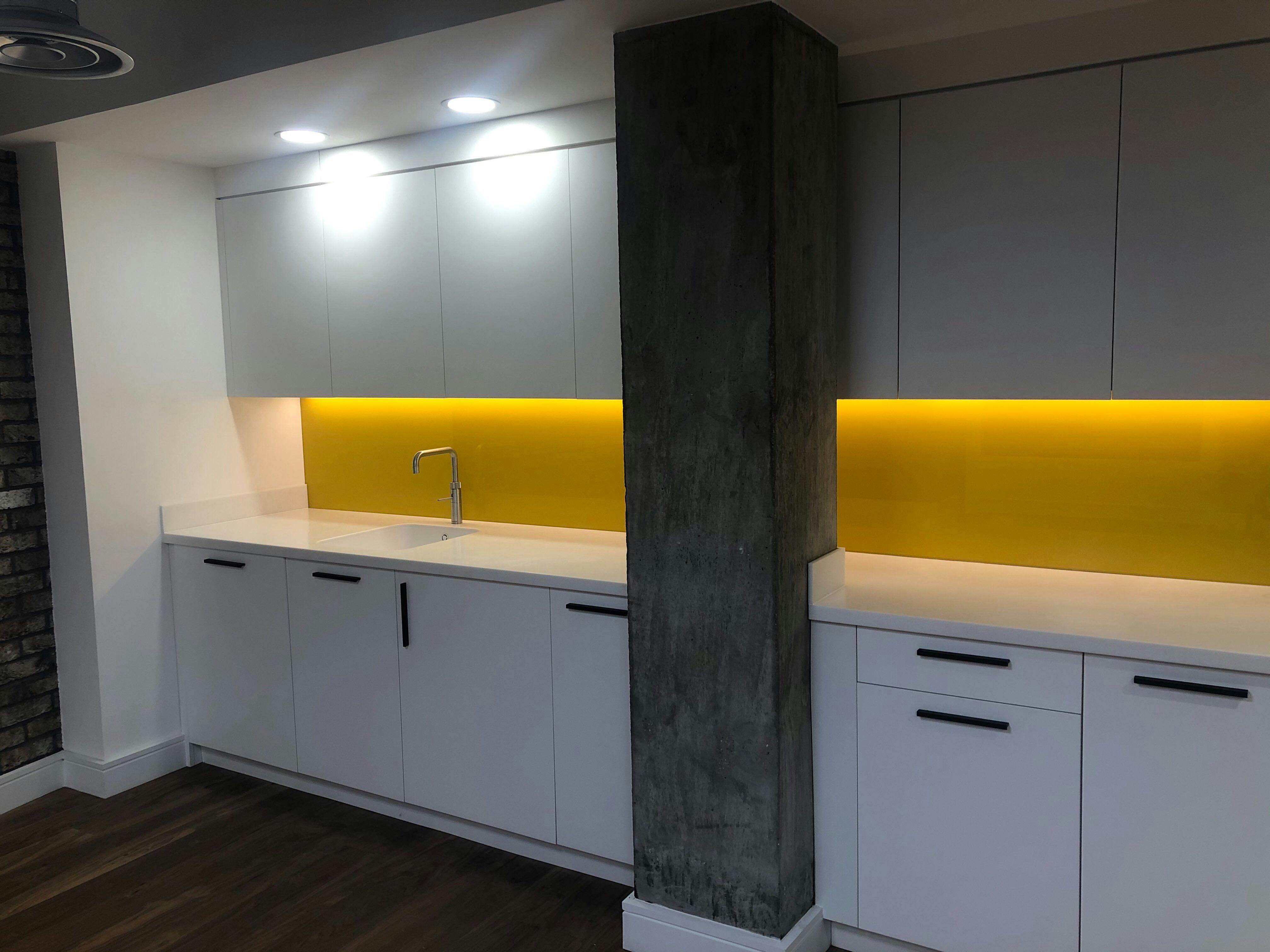 Modern kitchenette with white cabinetry and yellow backlight for events and meetings.