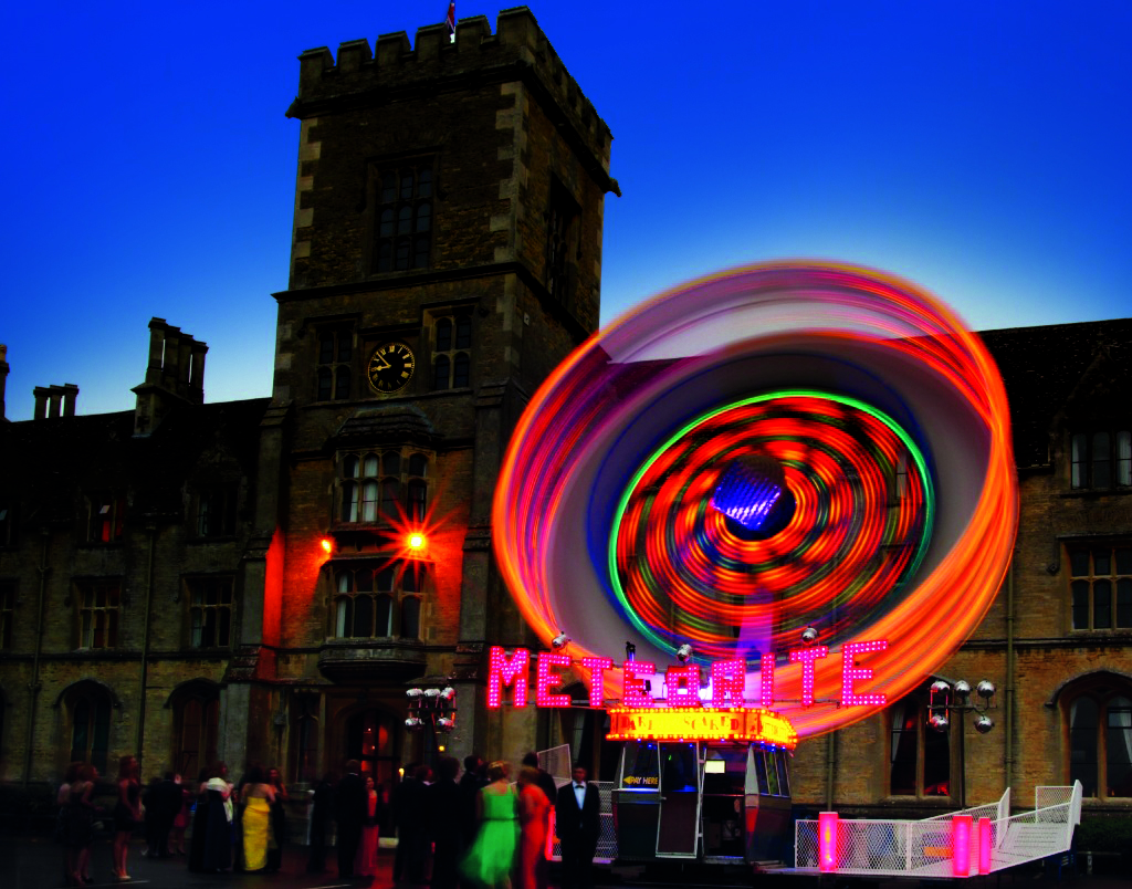 Vibrant outdoor event at Royal Agricultural University with spinning attraction and dynamic lighting. - Banner