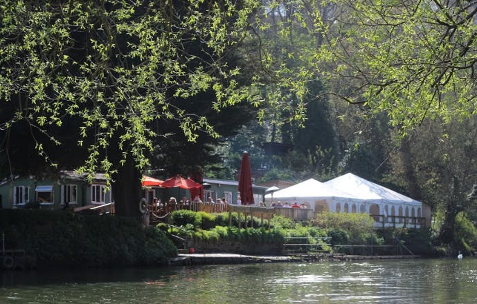 Lakeside outdoor venue with white tent and red umbrellas for events and meetings.