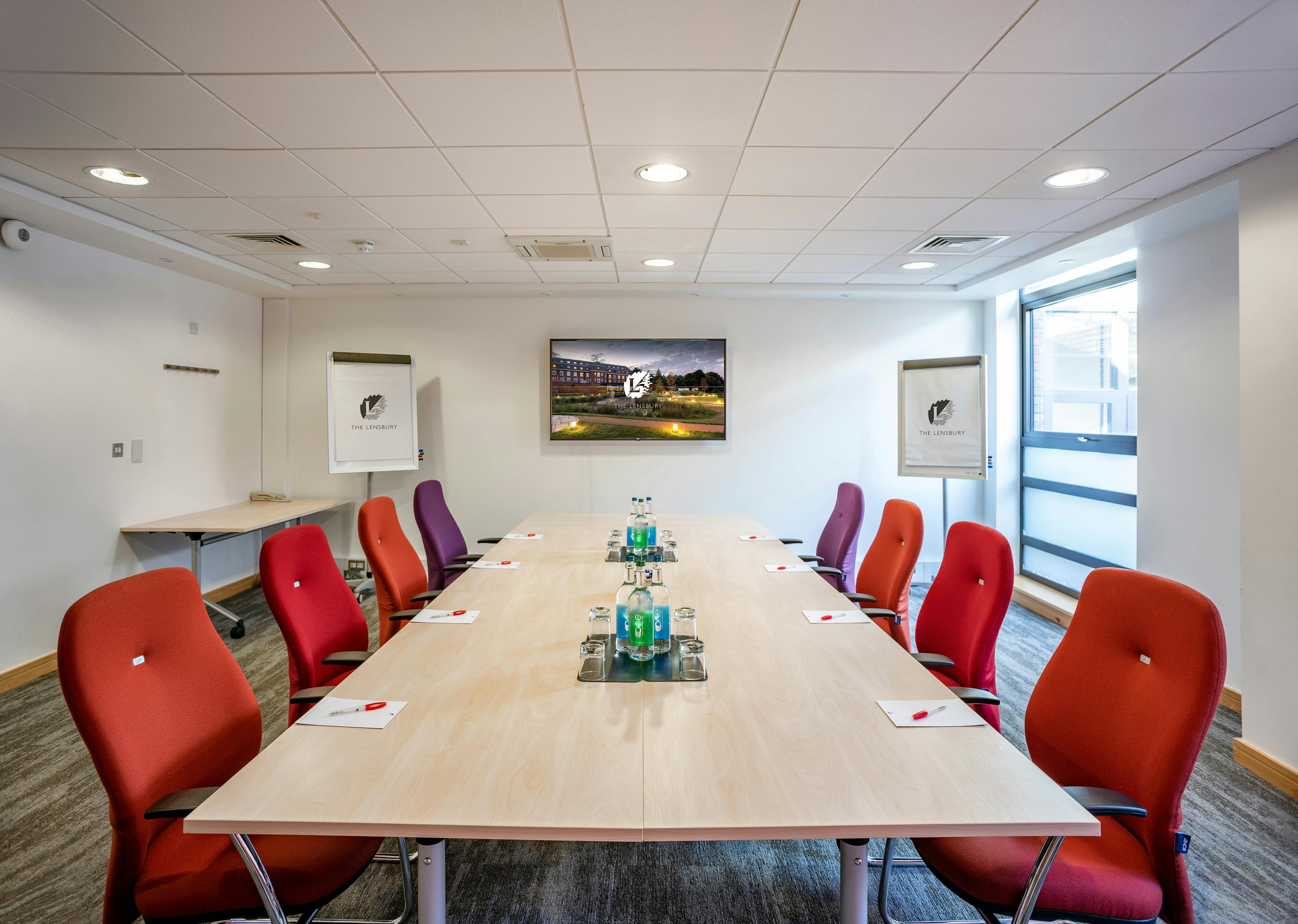 Modern meeting room at The Lensbury with vibrant chairs, ideal for conferences and brainstorming.