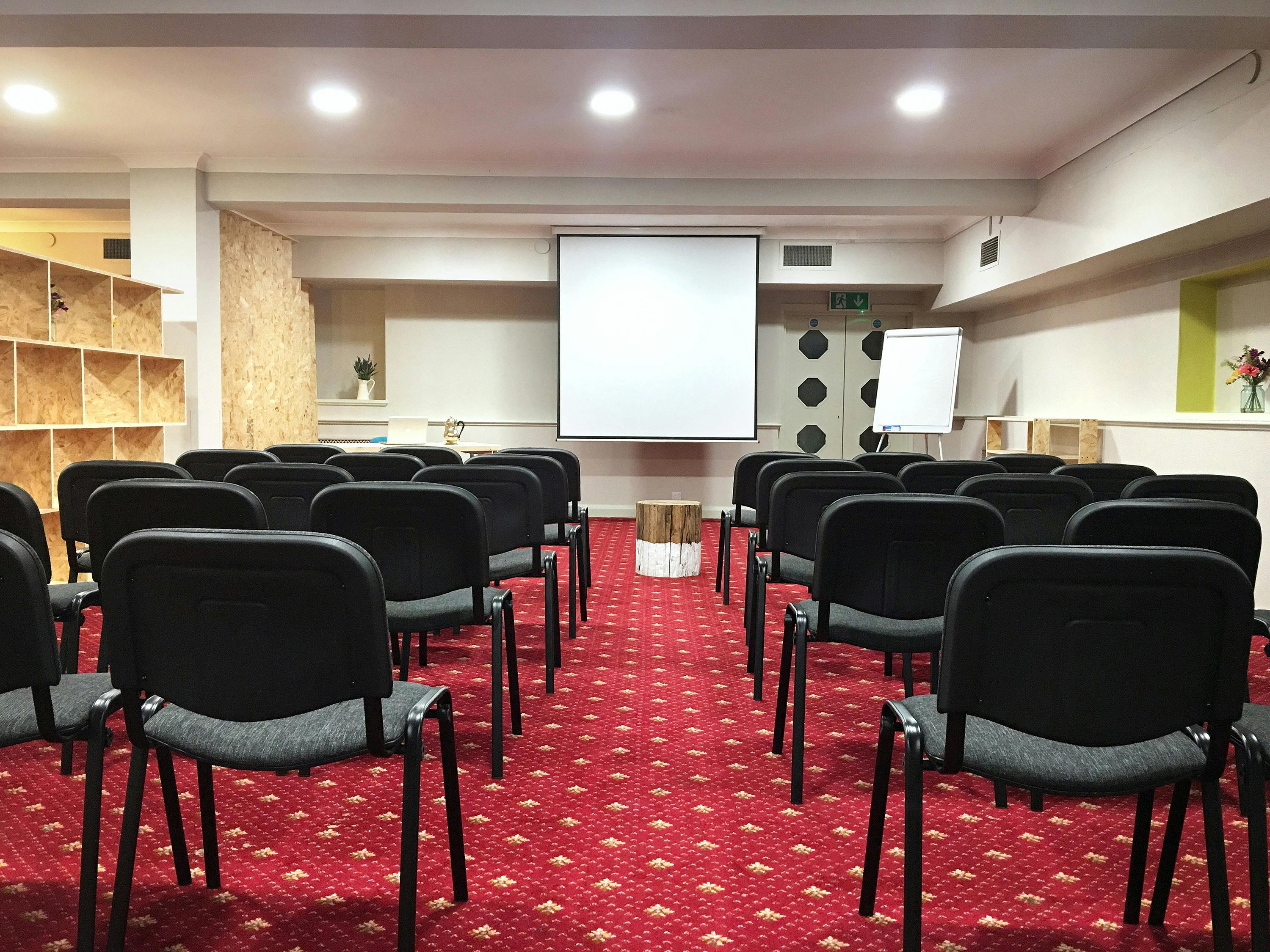 Meeting room with chairs and projection screen, ideal for workshops and conferences.