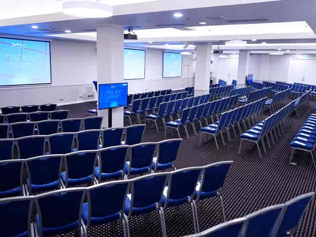 Daugava Ballroom conference setup with blue chairs and dual screens for events.