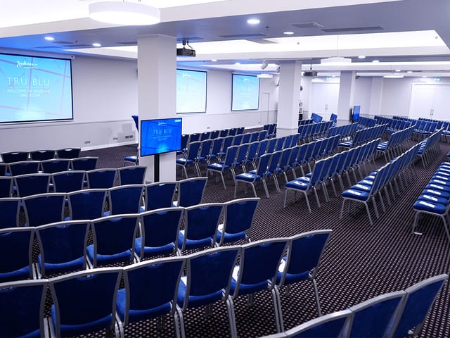 Daugava Ballroom conference setup with blue chairs and dual screens for events.