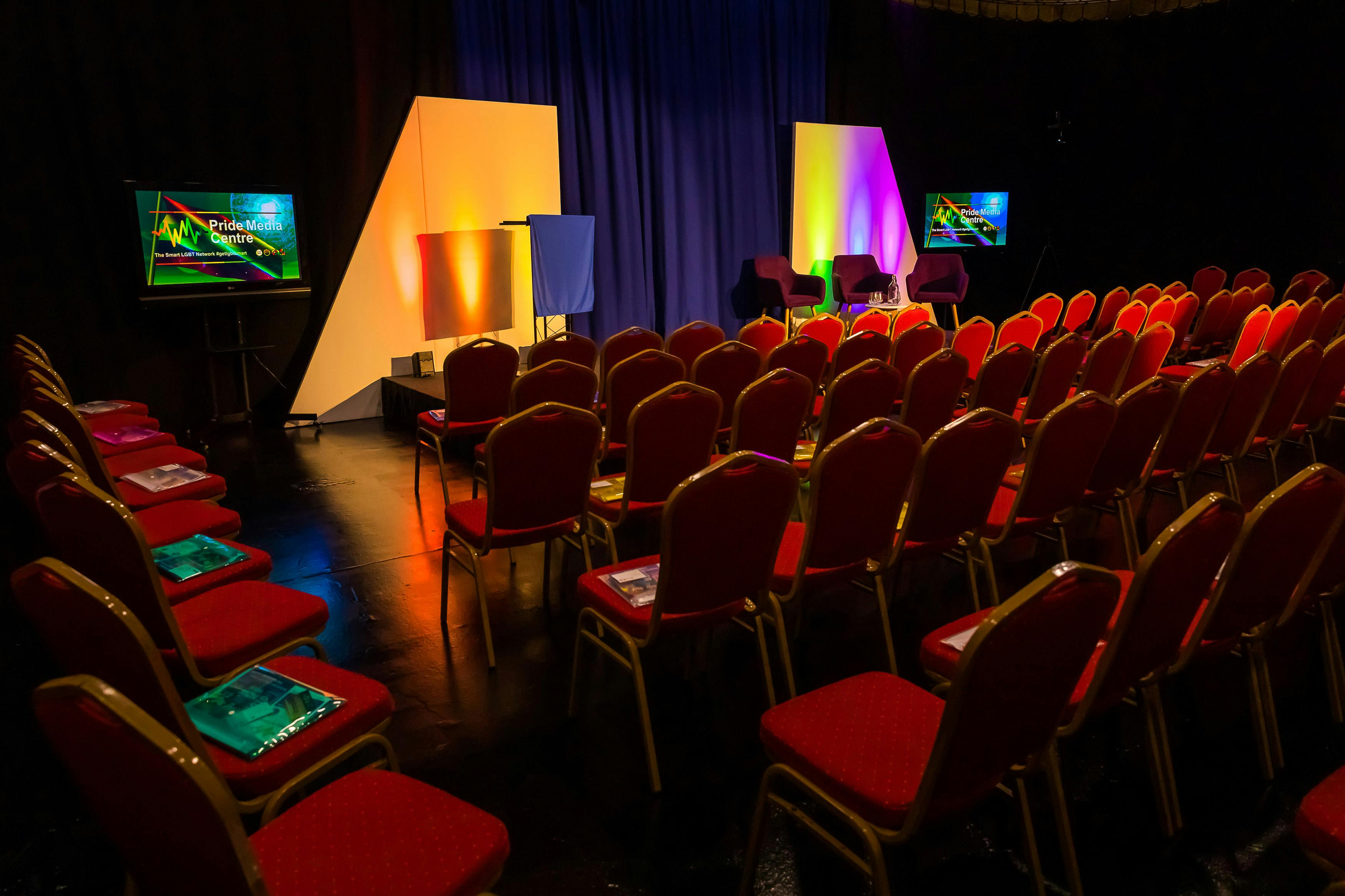 TV studio event space with vibrant lighting, red chairs for audience engagement, multimedia setup.