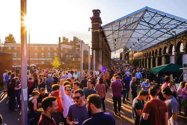 Vibrant outdoor networking event at The Carriage Shed with large crowd under open-air structure.