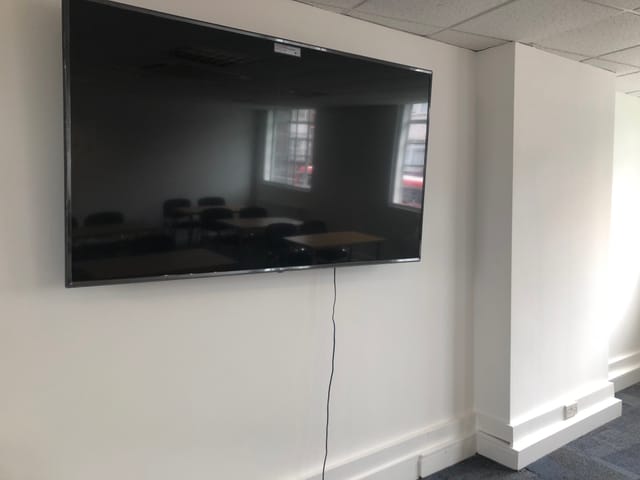 Modern seminar room with wall-mounted TV, ideal for presentations and video conferencing.