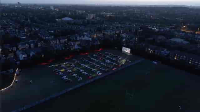 Drive-in movie setup at Sunset Cinema with large screen and parked cars for community events.