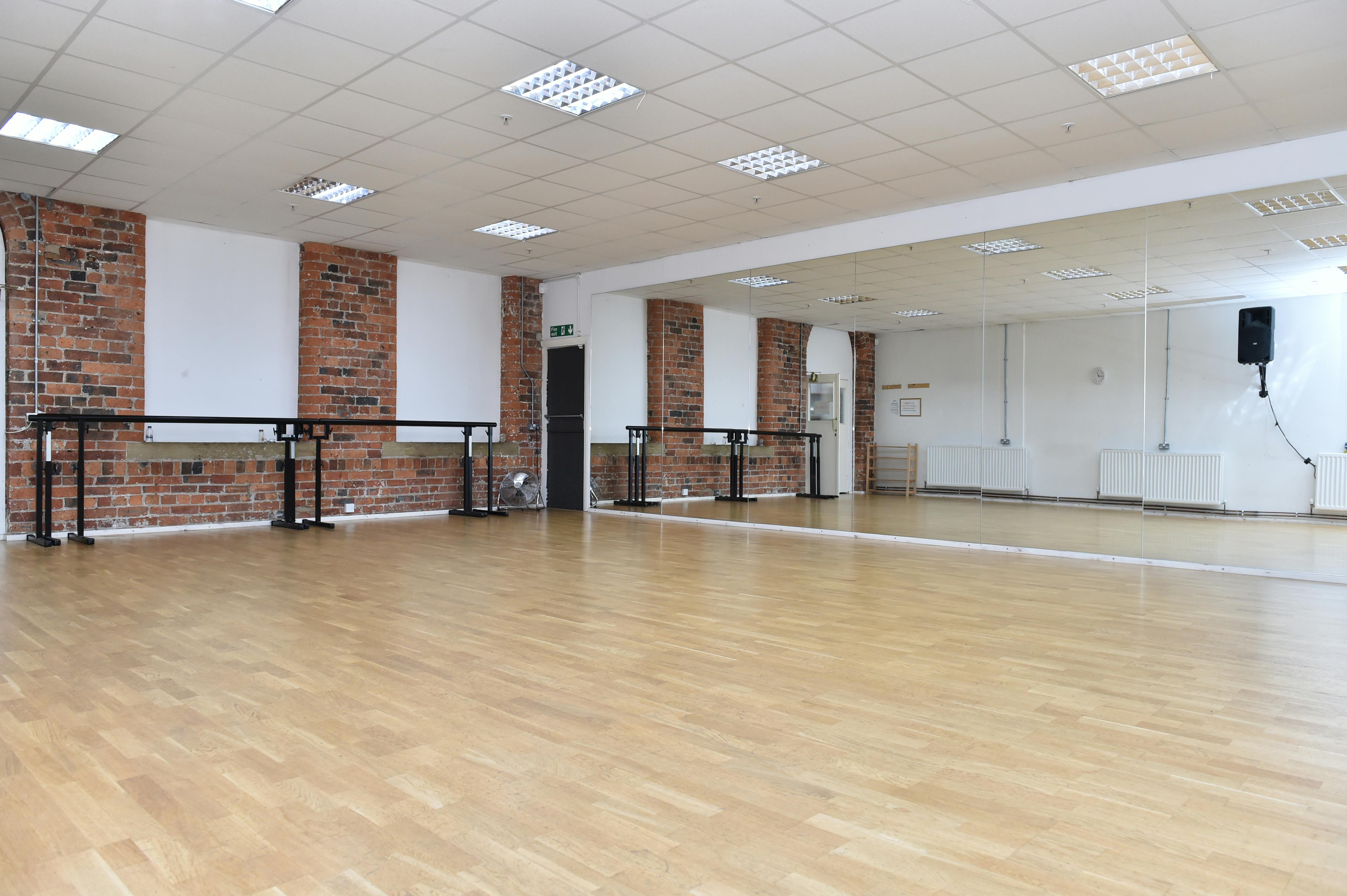 Spacious dance studio with wooden floors and mirrors, perfect for classes and workshops.