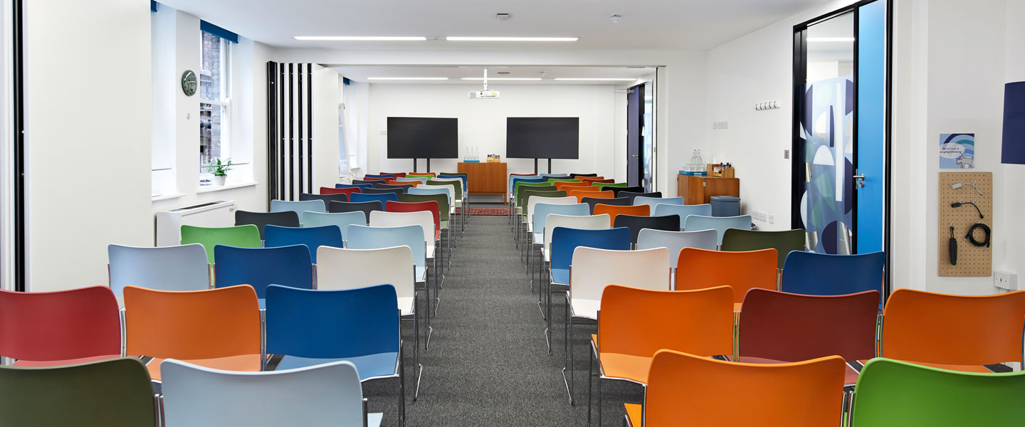 Flexible meeting space with colorful chairs, ideal for workshops and seminars. - Banner