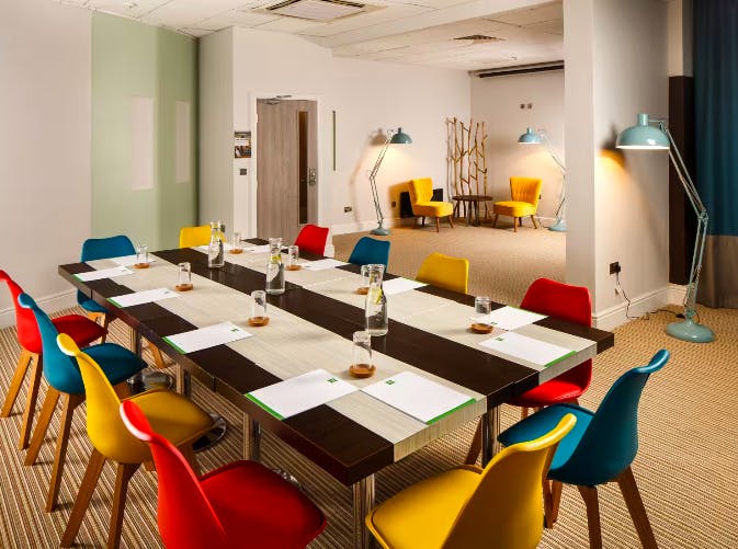 Thomas Shelby in a modern meeting room with colorful chairs for workshops.