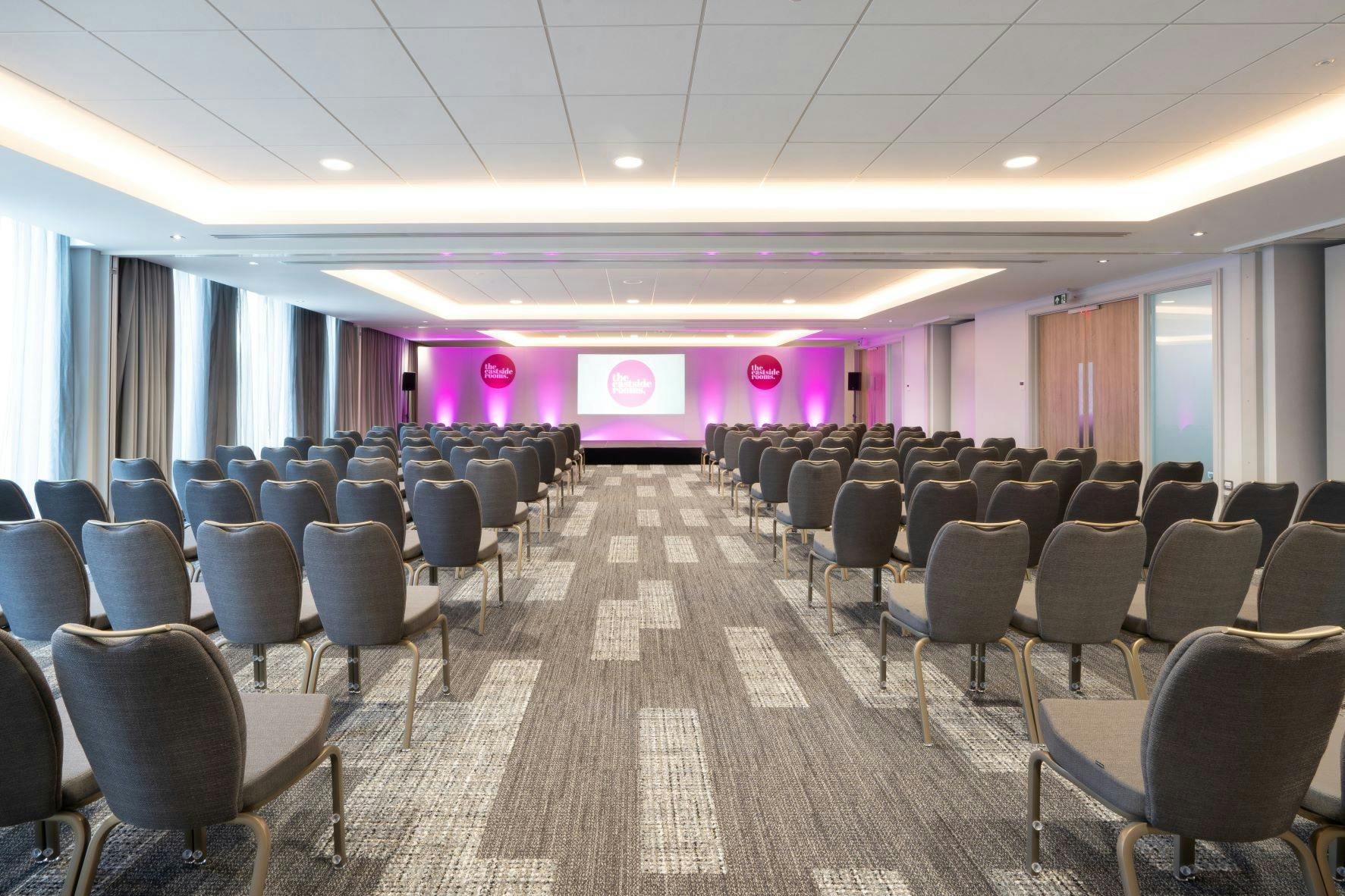 Conference room with comfortable chairs and pink accents for corporate events.