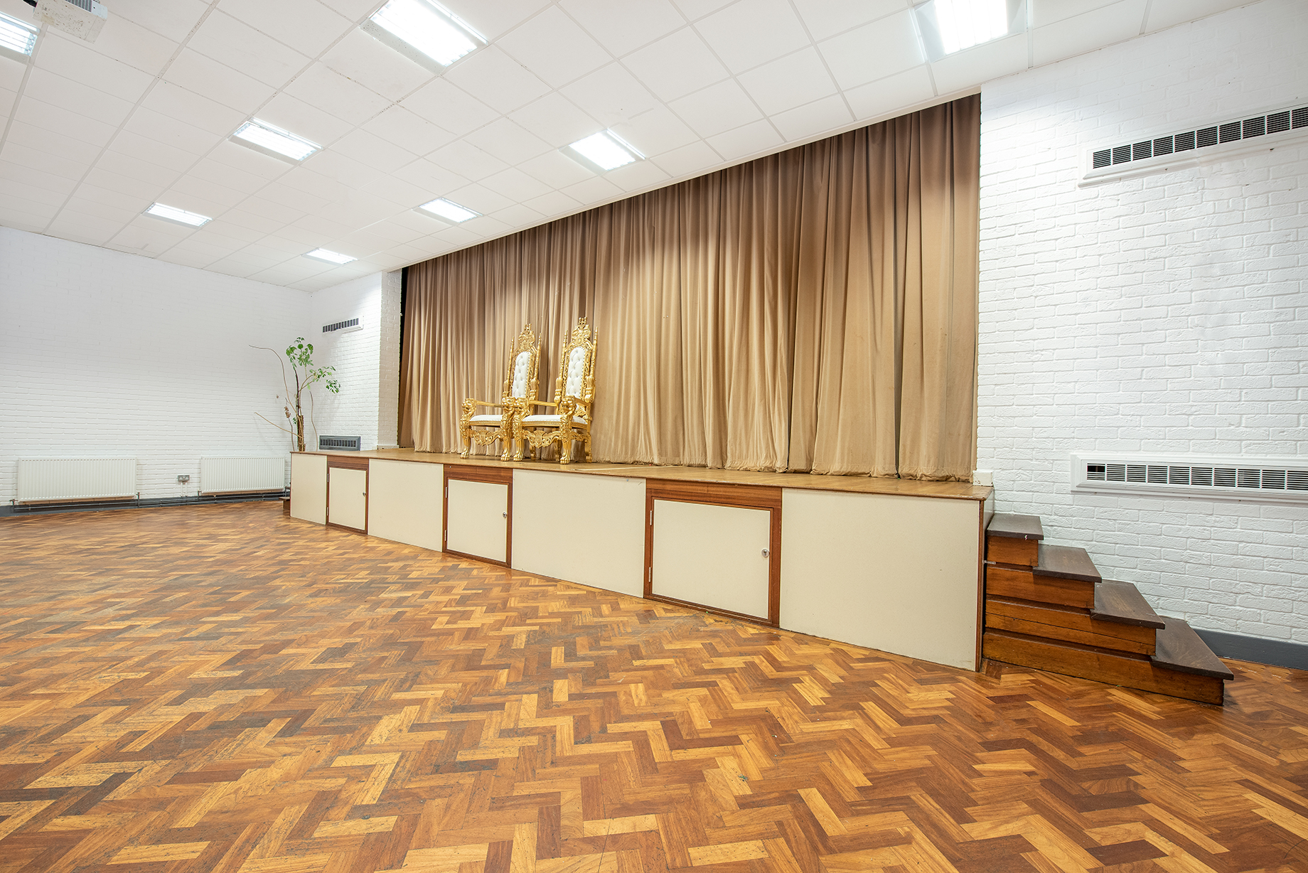 Versatile event space with raised stage and ornate chairs at St Georges Community Hub Hall.