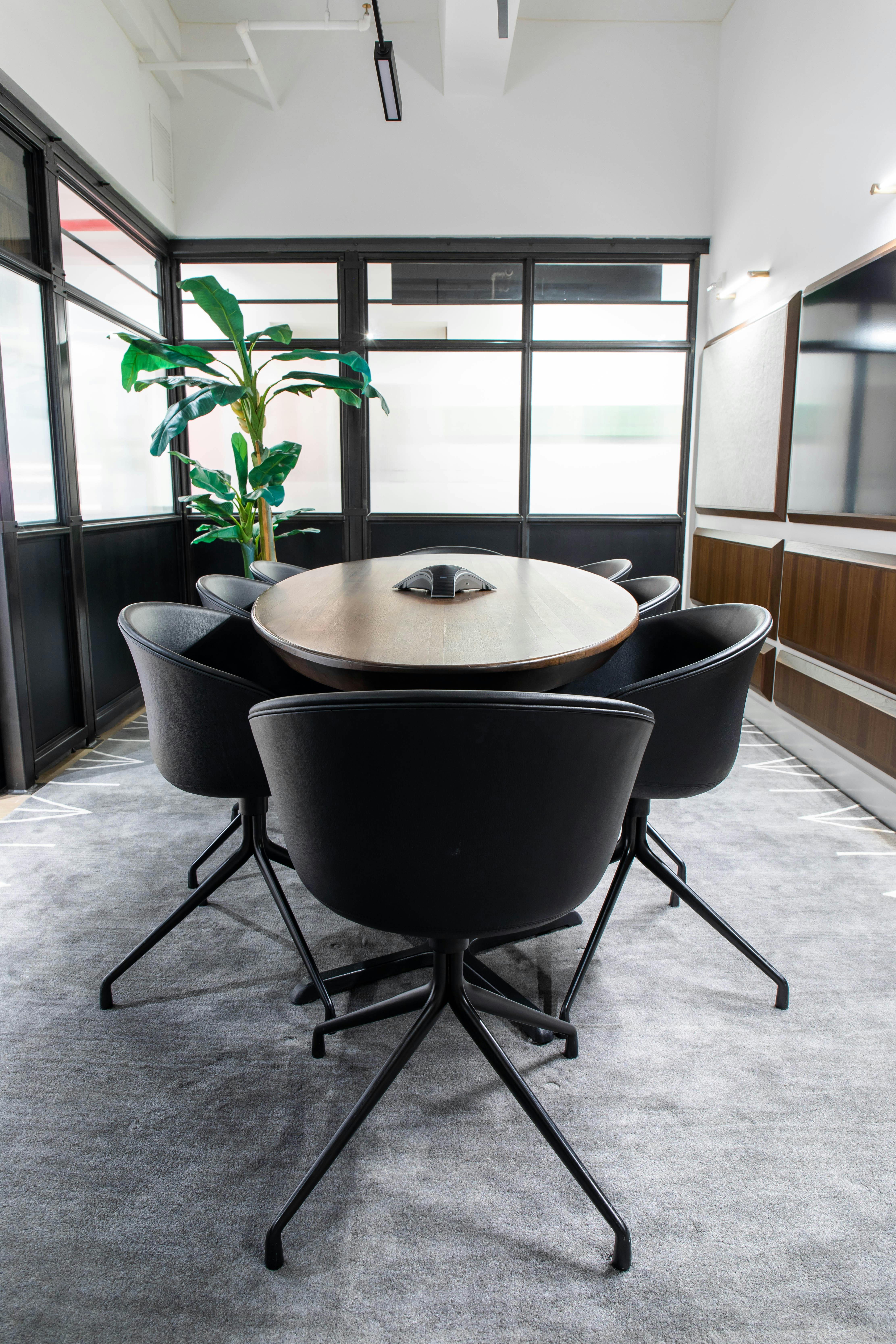 Modern conference room with round wooden table and sleek black chairs, ideal for meetings.