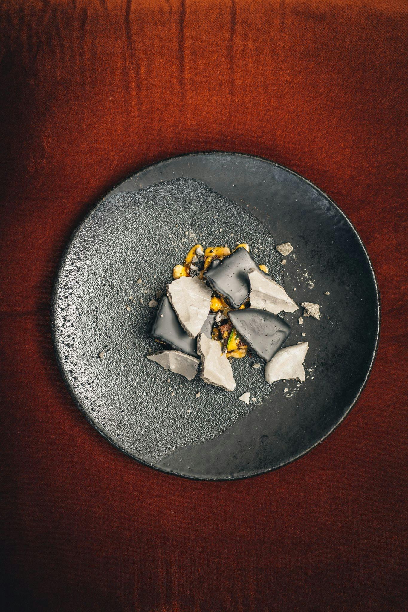 Meticulously plated dessert on dark plate, perfect for upscale events and dining experiences.