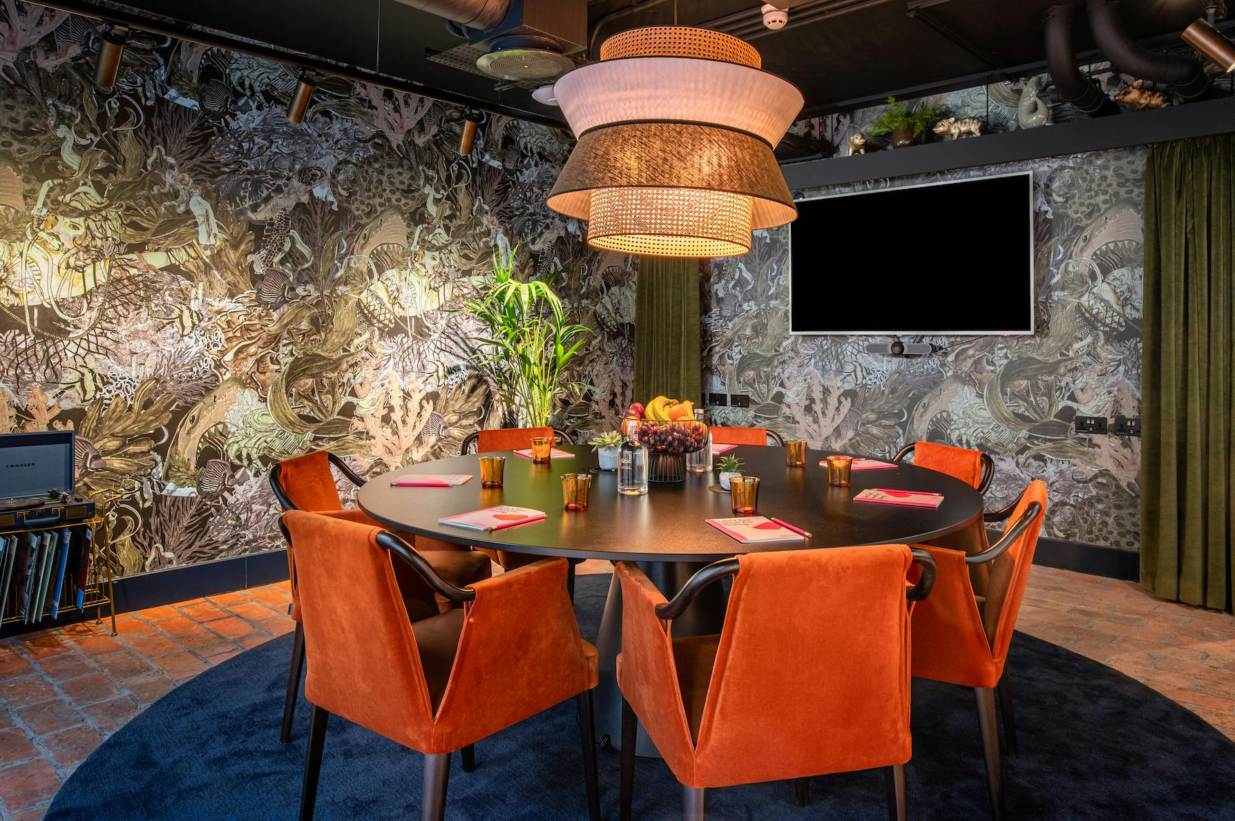 Stylish meeting room at Yotel Manchester with round table and vibrant orange chairs.