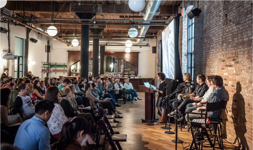 Panel discussion at Wythe Hotel's Main Hall with engaged audience and stylish decor.