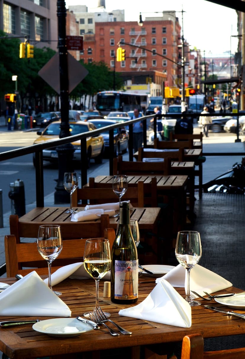 Outdoor dining area at Tribeca Grill, featuring wooden tables for casual networking events.
