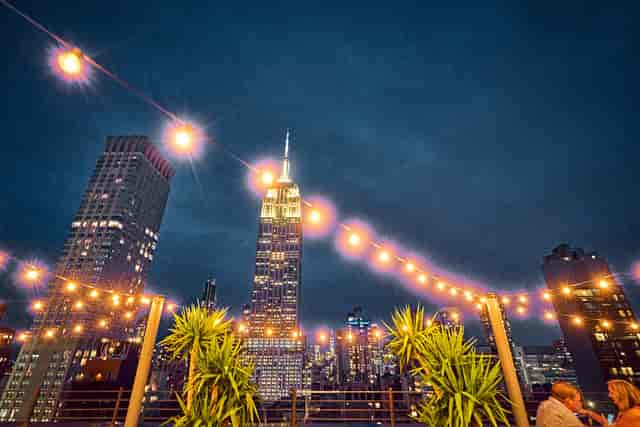 Rooftop venue with string lights and Empire State Building, ideal for upscale events.