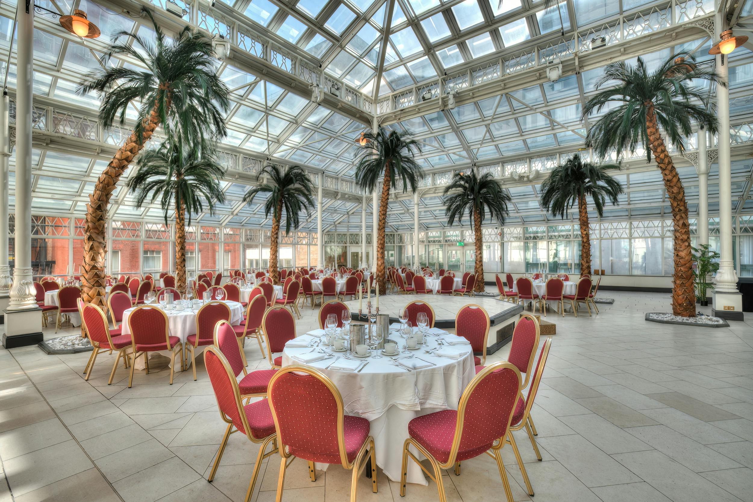 Elegant event space with round tables and palm trees in Millennium Gloucester, London.