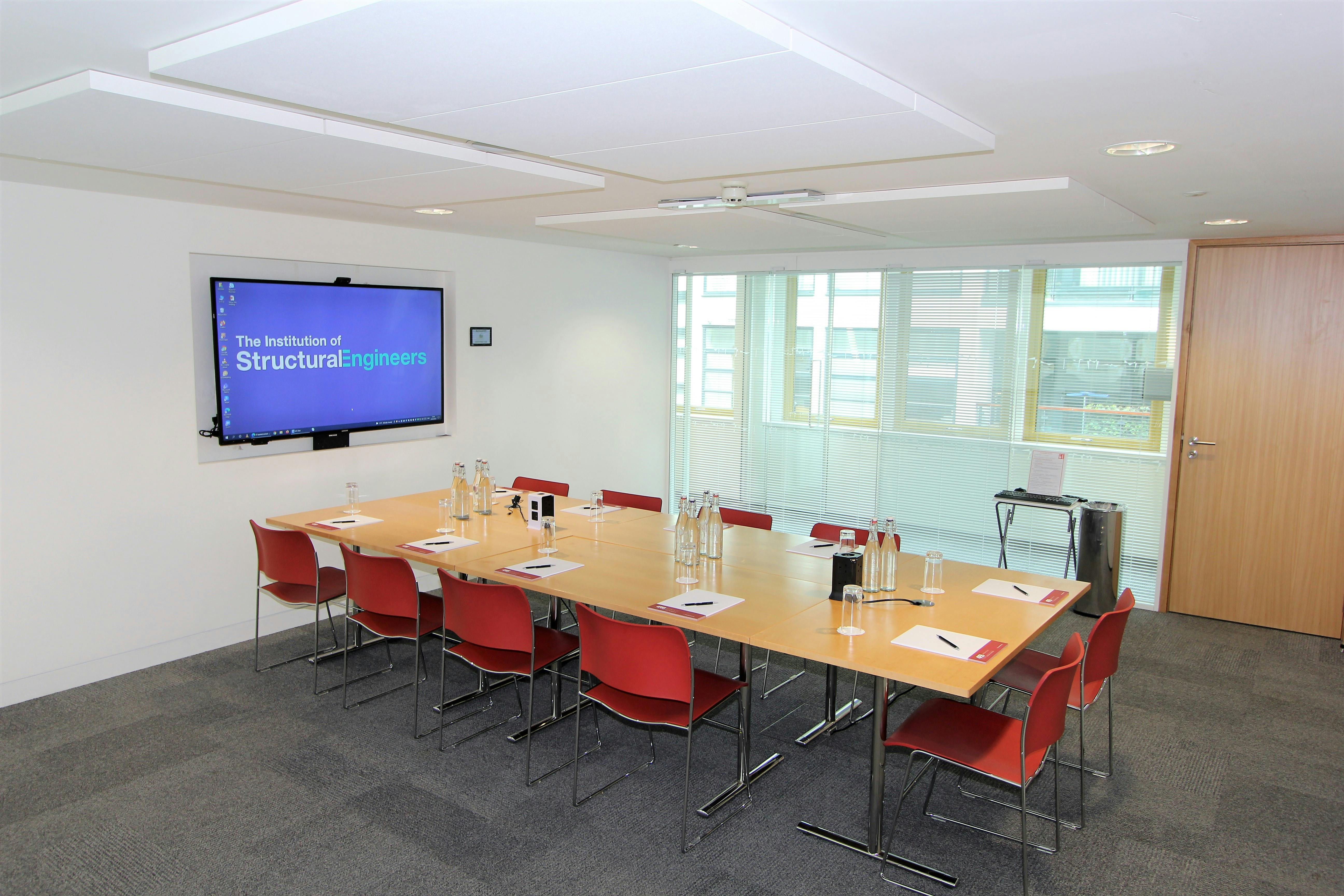 Modern meeting room with wooden table and red chairs, ideal for professional events.