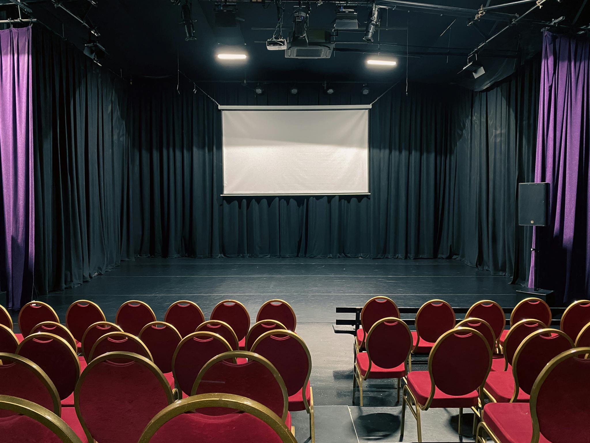 Versatile event space with red chairs and projection screen for presentations and workshops.