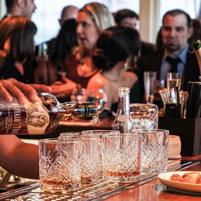 Lively networking event at Jackie-American Bistro with bartender pouring whiskey.