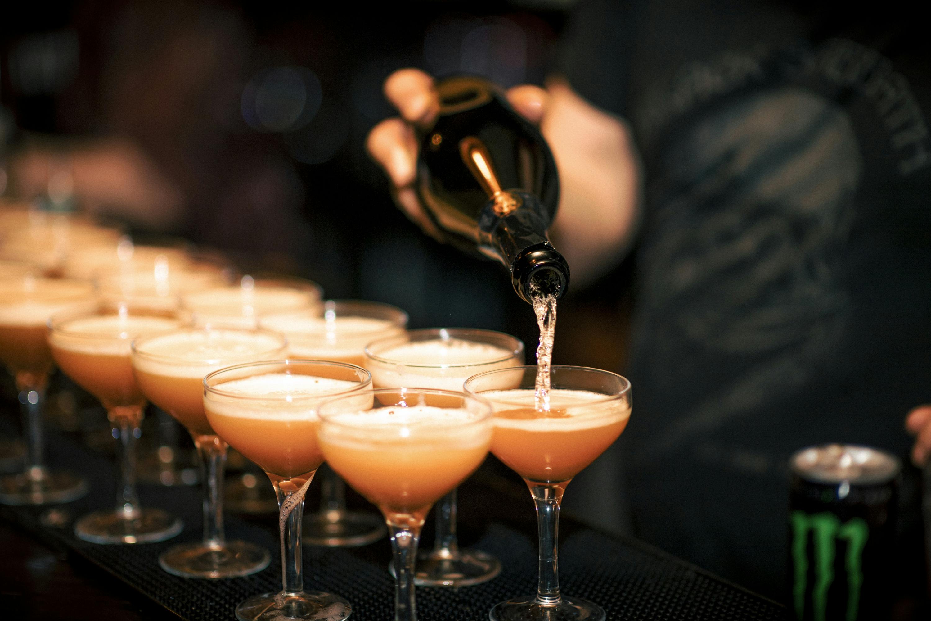 Bartender pouring cocktails into coupe glasses at The Cocktail Club Cardiff event.