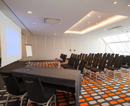 Meeting room in Hilton Paris La Defense with black chairs and projection screen for events.