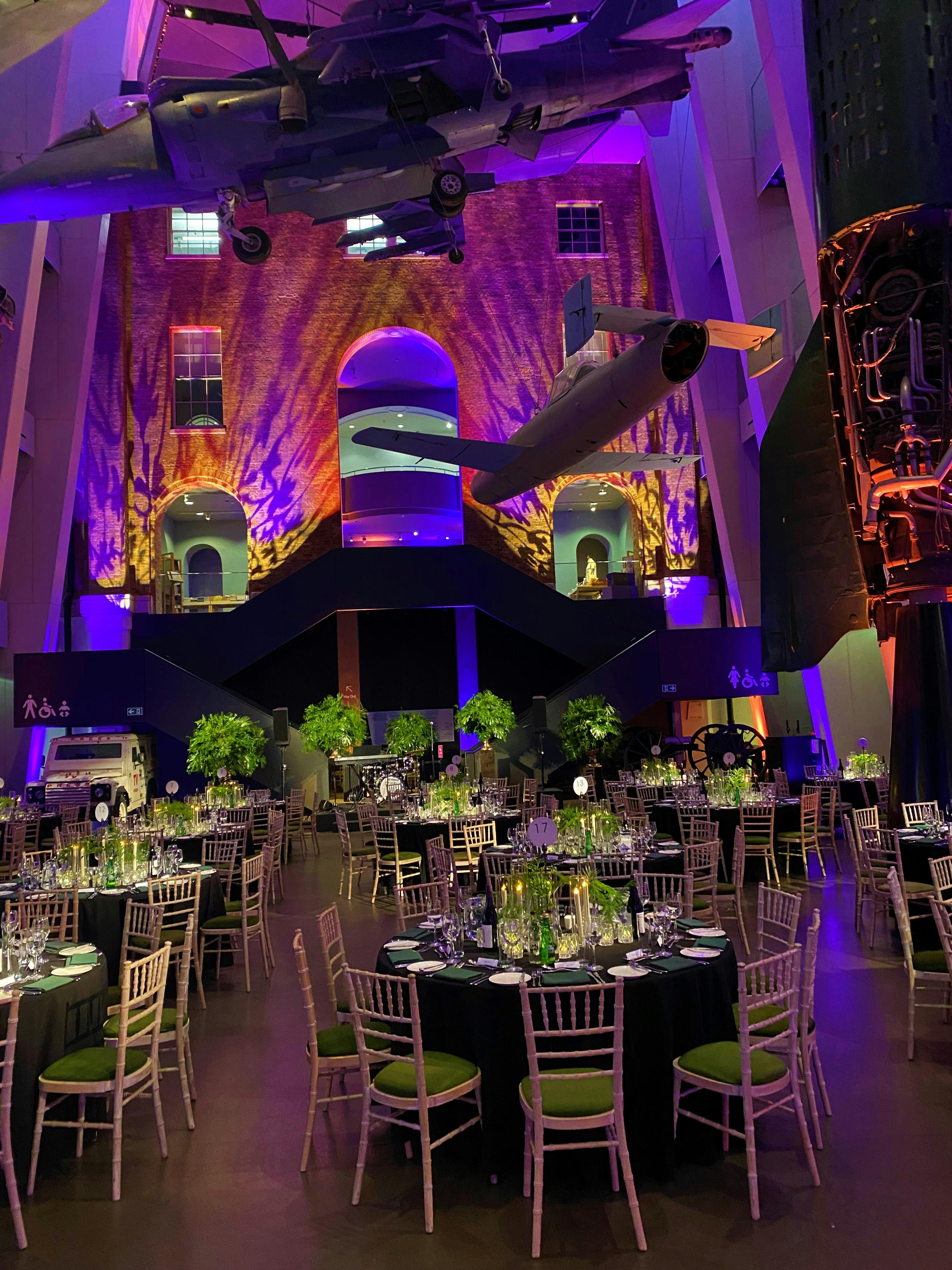 Atrium at IWM London with elegant tables and suspended aircraft for events.