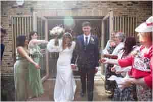Joyful wedding couple exiting The Glass House, surrounded by confetti and smiling guests.