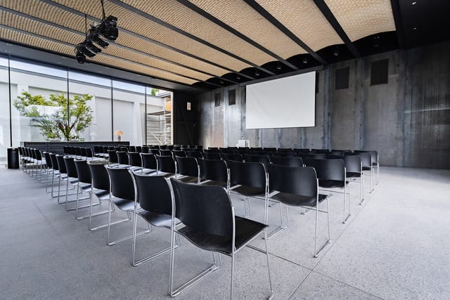 Modern event space in Mogens Dahl Koncertsal with black chairs and projection screen.