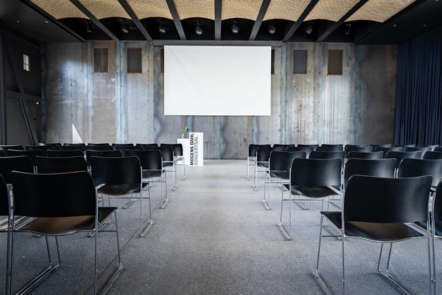 Modern event space with black chairs and large screen, ideal for conferences and workshops.