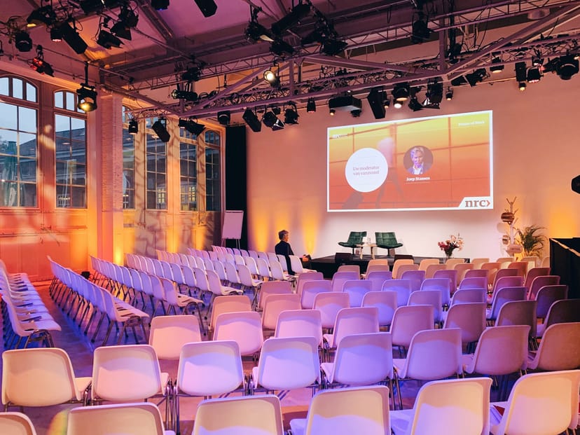 Modern event space with white chairs, ideal for presentations and panel discussions.