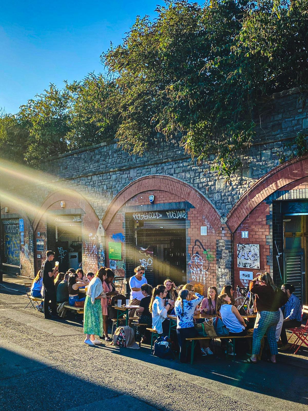 Vibrant outdoor networking at The Cider Box with communal tables and urban backdrop.