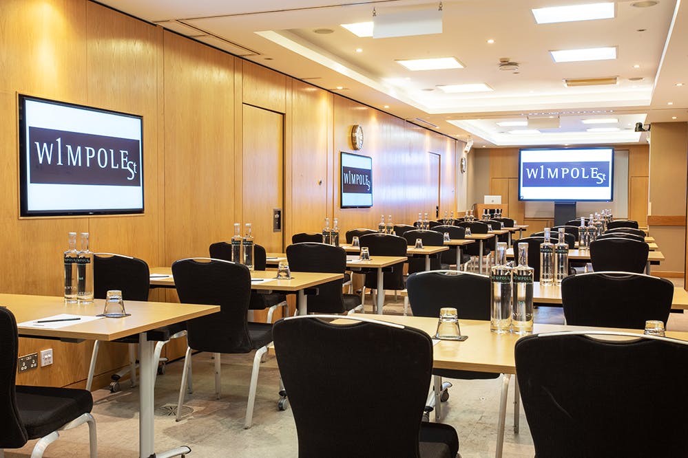 Corporate meeting room with classroom setup, dual screens, and warm wood paneling.