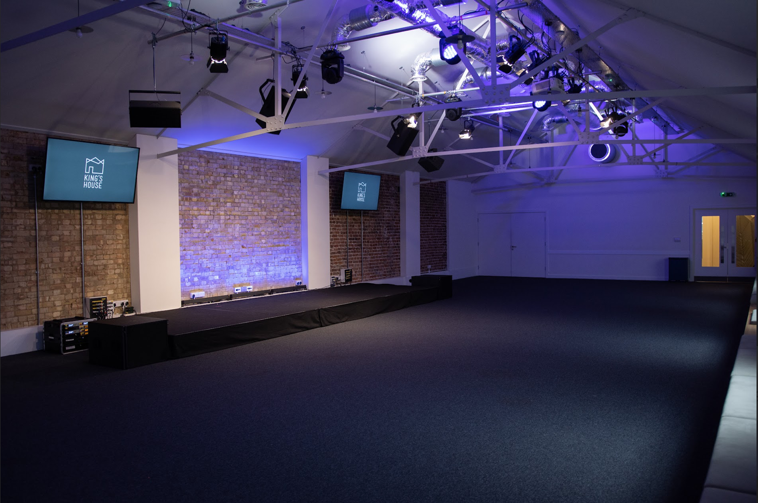 Versatile event space in King's House with raised stage for presentations and performances. - Banner