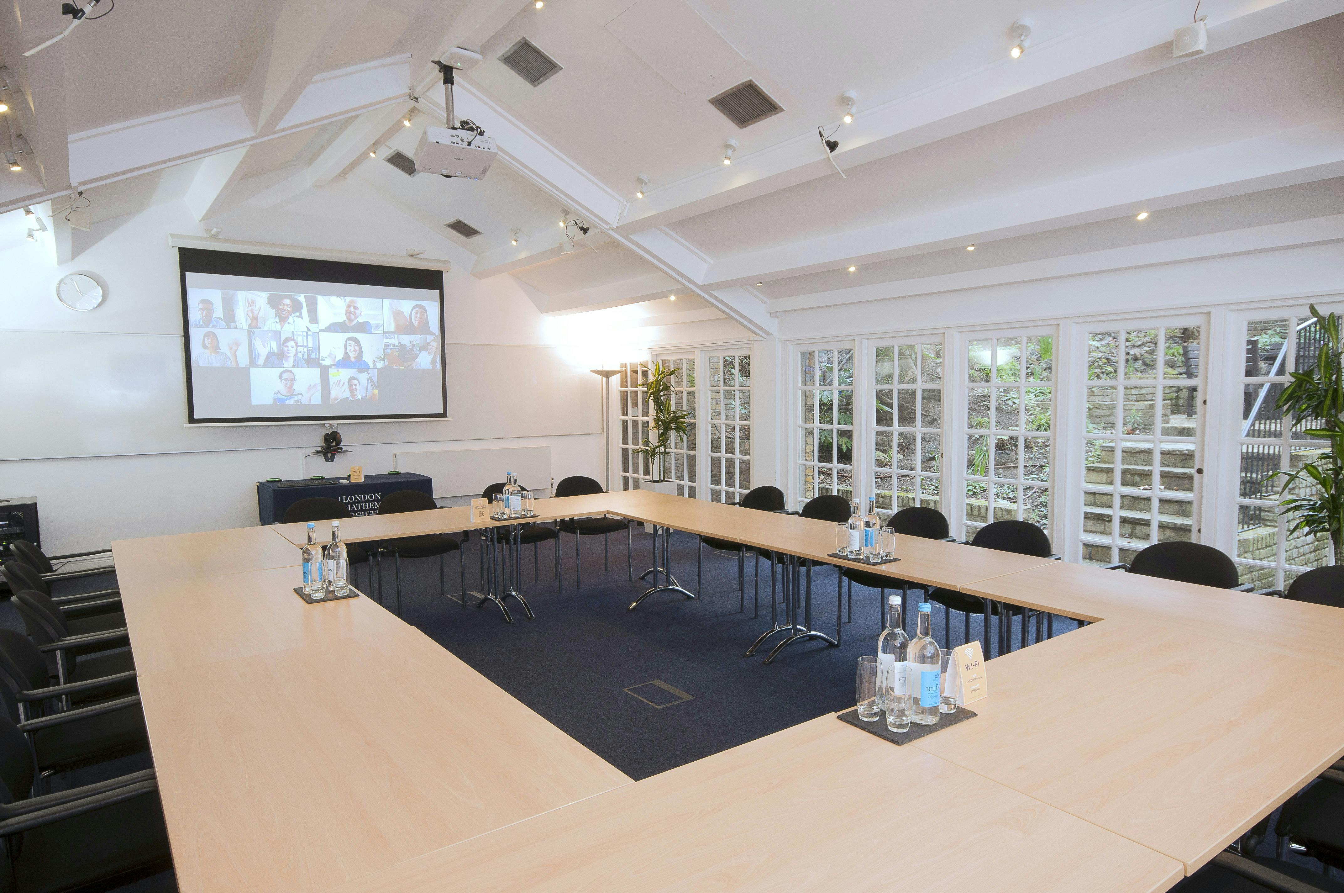 Hardy Room in De Morgan House, hybrid meeting space with central table and projector screen.